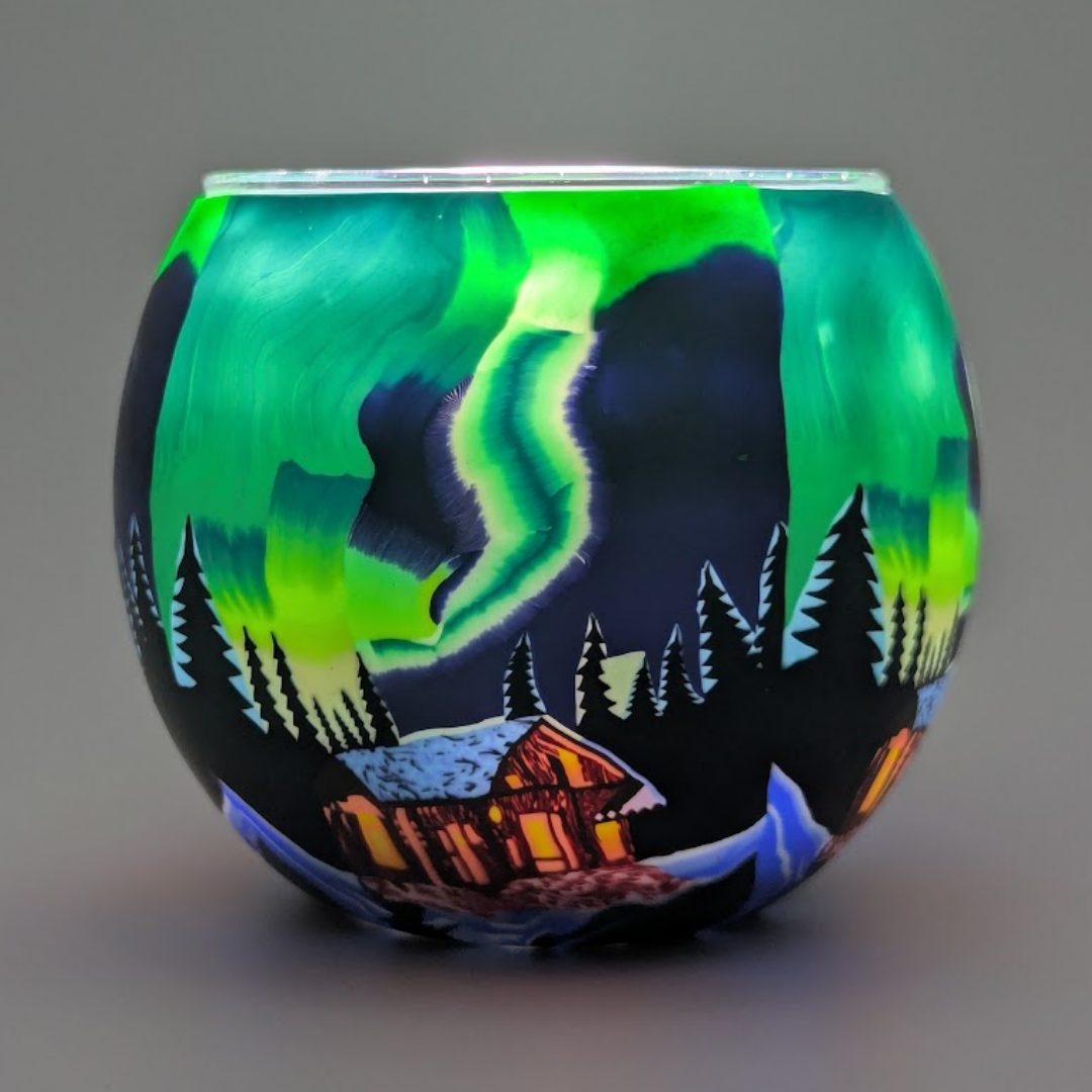 Glass light globe with a design of the Northern Lights over a cabin in the woods. Over a dark background.